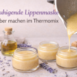 Beruhigende DIY-Lippenmaske mit Lavendel wird aus dem Thermomix in kleine Glastiegel abgefüllt; Lavendelblüten, Honig und Öl liegen auf einer hellen Arbeitsfläche.